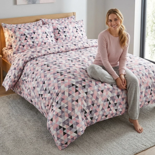 Kobieta relaksująca się na łóżku z kolorową, wygodną pościelą bawełnianą J&W we wzór geometrycznych trójkątów.