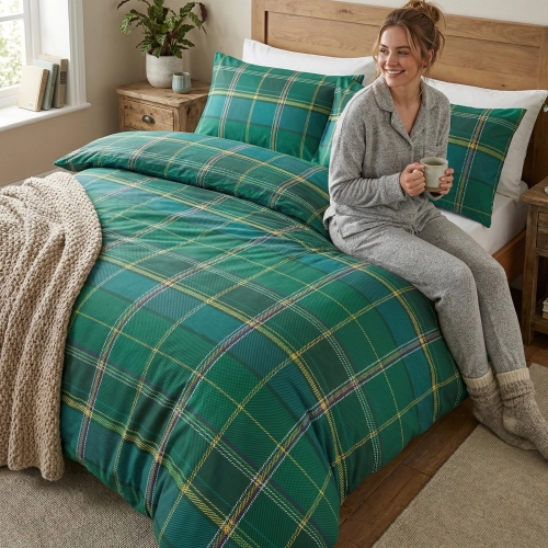 Kobieta relaksująca się na łóżku z zieloną pościelą z bawełny J&W we wzór kraty.