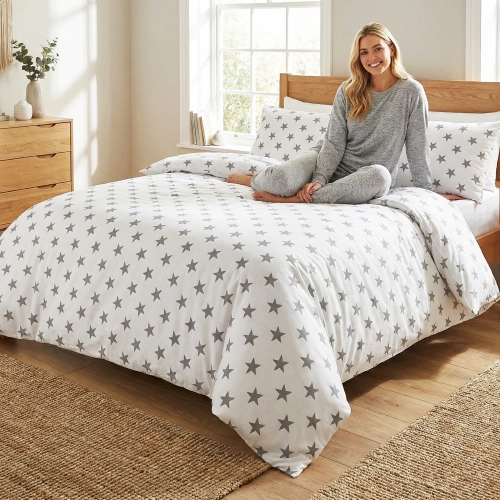 Kobieta relaksująca się na łóżku z białą, wygodną pościelą bawełnianą J&W we wzór szarych gwiazd.