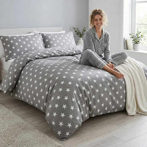 Kobieta relaksująca się na łóżku z szarą, wygodną pościelą bawełnianą J&W we wzór białych gwiazd.