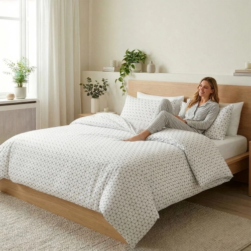 Kobieta siedząca na łóżku z pościelą w szare geometryczne heksagony