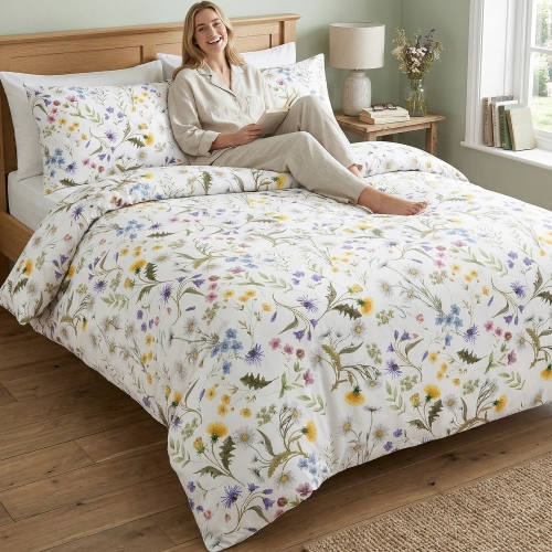 Kobieta relaksująca się na łóżku z jasną, wygodną pościelą bawełnianą J&W we wzór letnich, polnych kwiatów.