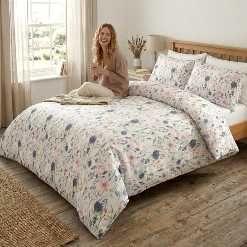 Kobieta z herbatą relaksująca się na łóżku z jasną, wygodną pościelą bawełnianą J&W we wzór letnich, polnych kwiatów i z