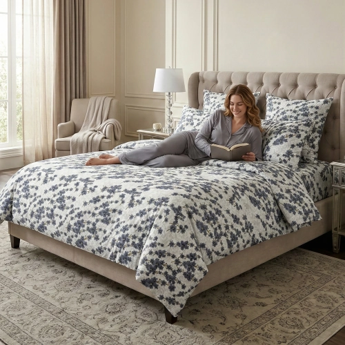 Uśmiechnięta kobieta czytająca książkę w eleganckiej sypialni na łóżku w pościeli w granatowe kwiaty z kolekcji Nocny Og