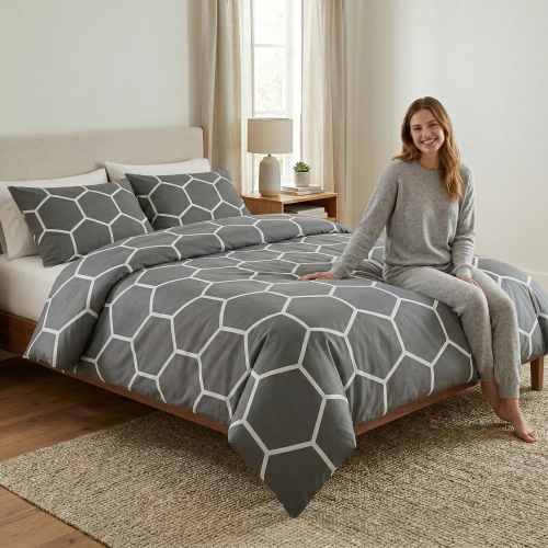 Uśmiechnięta kobieta siedząca na drewnianym łóżku w szarej pościeli w geometryczny wzór Szary Heksagon marki J&W