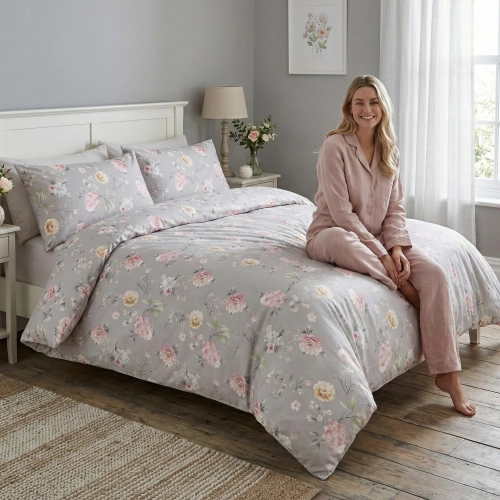 Uśmiechnięta kobieta w różowej piżamie siedząca na łóżku w pościeli w kwiaty z kolekcji Szare Peonie