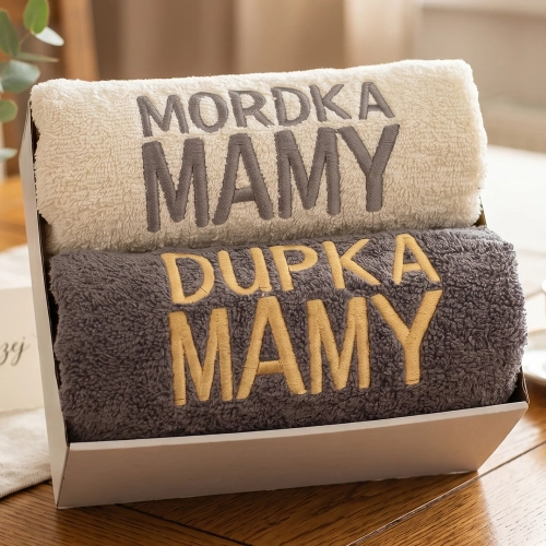 Zestaw prezentowy dwóch ręczników z haftem Mordka Mamy i Dupka Mamy w kolorze kremowym i stalowym ułożony na drewnianym