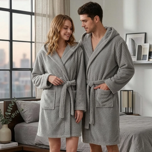 Uśmiechnięta para w sypialni ubrana w grube jasnoszare szlafroki kąpielowe z kapturem z miękkiej mikrofibry