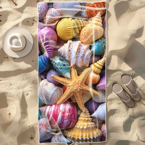 Duży ręcznik plażowy XXL z mikrofibry ze wzorem wielokolorowych muszli i rozgwiazdy, rozłożony na piasku obok kapelusza
