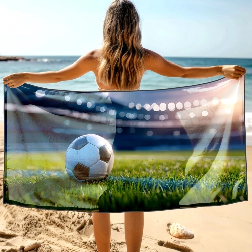 Kobieta tyłem trzymająca rozłożony duży ręcznik XXL z piłką nożną na tle oceanu