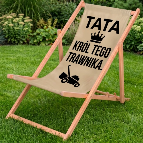 Drewniany leżak ogrodowy w kolorze cappuccino na zielonym trawniku z nadrukiem TATA KRÓL TEGO TRAWNIKA. i kosiarką, tło