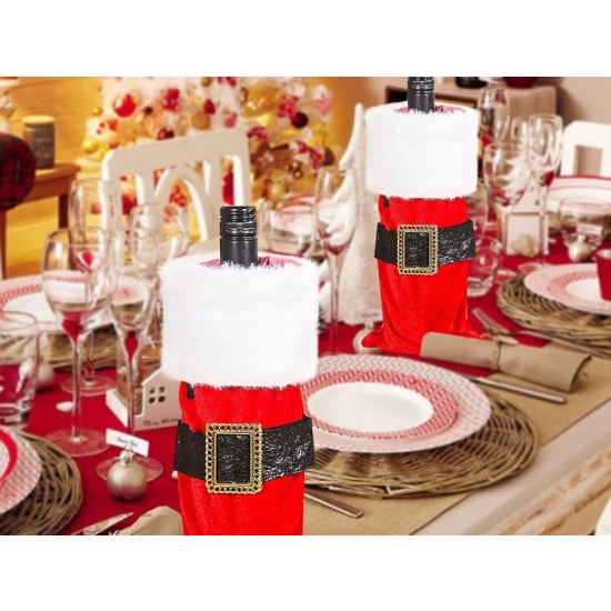 Butelka w pokrowcu Mikołaja, ustawiona na stole wigilijnym obok talerzy i świątecznych serwetek.