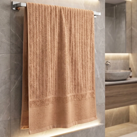 Brzoskwiniowy ręcznik bawełniany ARIA o strukturze w prążki wiszący na srebrnym wieszaku przy umywalce.