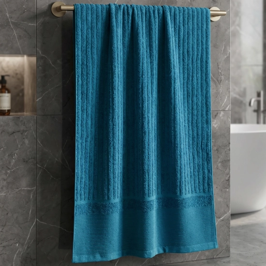 Morski turkusowy ręcznik ARIA prążkowany na złotym wieszaku w szarej marmurowej łazience z wanną.