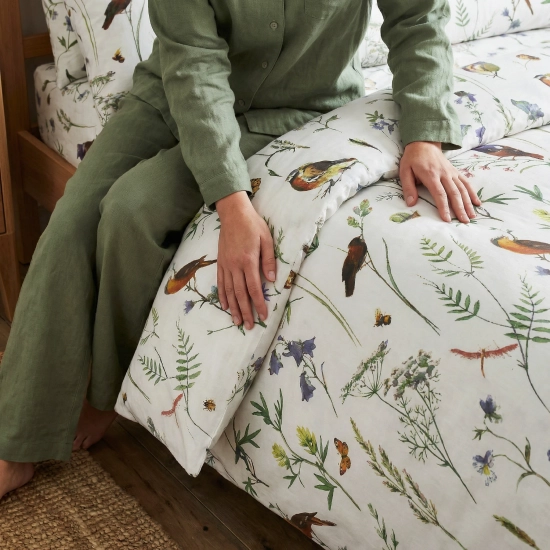 Zbliżenie rąk kobiety w zielonej piżamie, gładzących pościel we wzór botaniczny Łąka Botaniczna.