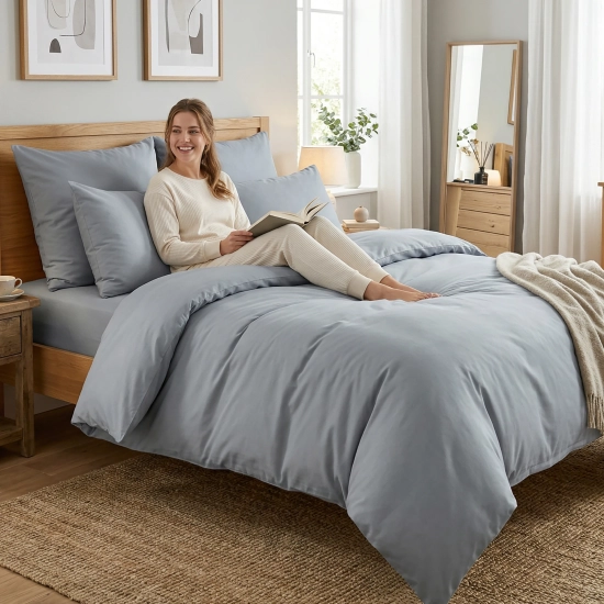 Kobieta czyta książkę w łóżku obleczonym w jasnoszarą pościel z bawełny premium J&W.