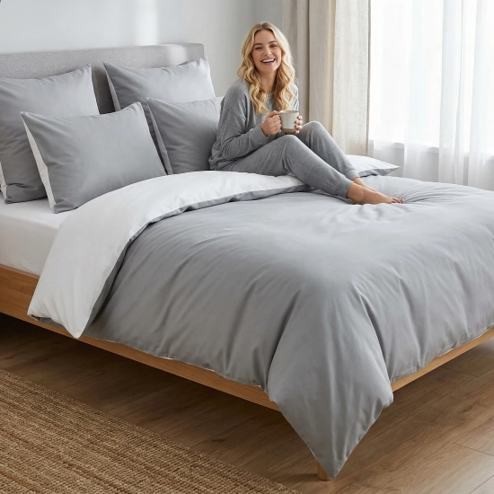 Uśmiechnięta kobieta relaksuje się w łóżku z dwustronną, jasnoszaro-białą pościelą J&W.