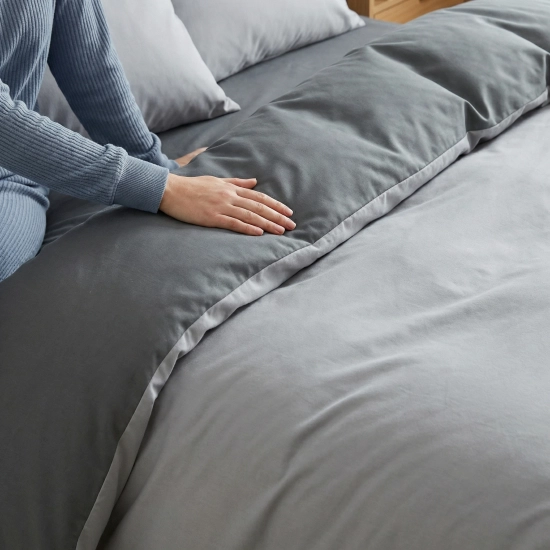 Zbliżenie dłoni na gładkim materiale dwustronnej pościeli J&W, widoczny kontrast dwóch odcieni szarości.