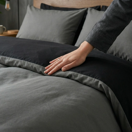 Zbliżenie dłoni na gładkim materiale dwustronnej pościeli J&W, widoczny kontrast ciemnej szarości i czerni.