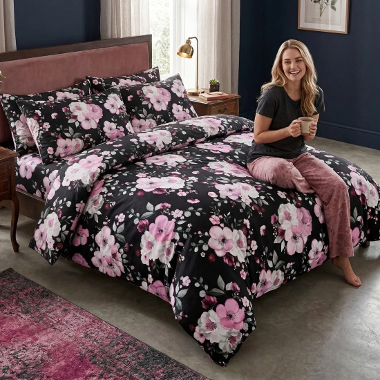 Uśmiechnięta kobieta w ciemnej piżamie siedzi na łóżku z luksusową, kwiatową pościelą z bawełny premium J&W z motywem ja