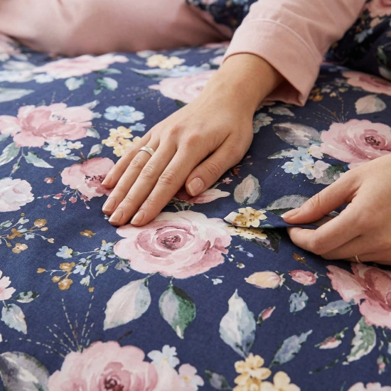 Zbliżenie na dłoń i detal miękkiego, gęstego materiału bawełnianej pościeli J&W zdobionej różowymi różami.