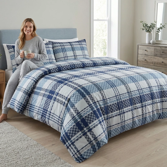 Łóżko w pełnej światła sypialni, zaścielone w elegancką pościel bawełnianą J&W we wzór szerokiej, niebieskiej kraty.