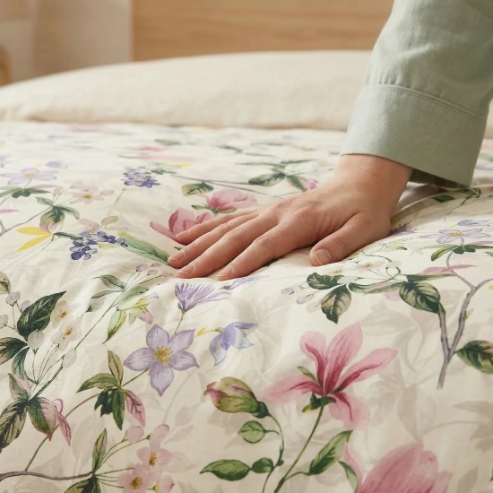 Zbliżenie dłoni na miękki materiał pościeli z malarskim wzorem kwiatów wiśni