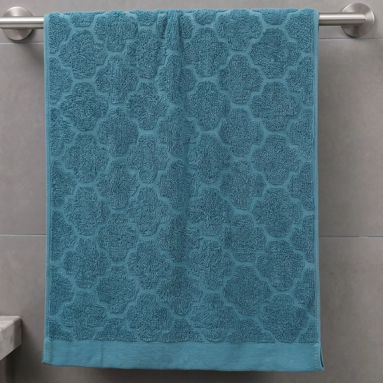 Morski (turkusowy), klasyczny ręcznik bawełniany Fiamo 50x100 w żakardowy geometryczny wzór, wiszący na stalowym relingu ściennym.
