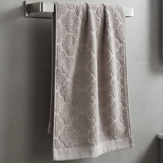 Jasnobeżowy (kremowy) ręcznik do rąk i twarzy z kolekcji Fiamo 50x100 w elegancki wzór, powieszony na wieszaku w jasnej łazience.