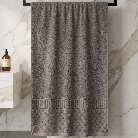 Szaro-brązowy bawełniany ręcznik z tłoczonym wzorem i żakardową bordiurą wiszący na czarnym wieszaku w jasnej łazience