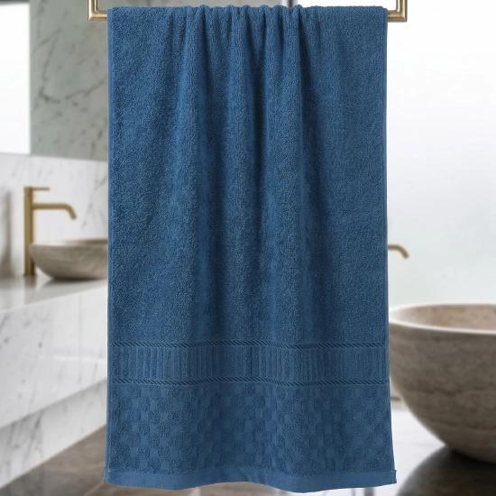 Granatowy ręcznik łazienkowy 50x100 cm z bordiurą wiszący na wieszaku w nowoczesnej łazience z kamienną wanną