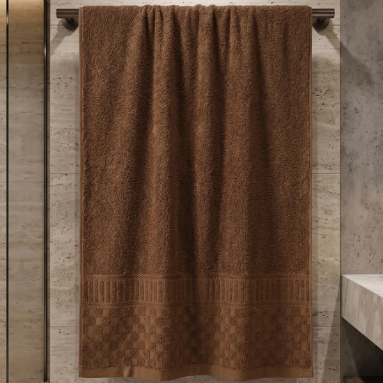 Czekoladowo-brązowy ręcznik bawełniany Fresco z żakardową bordiurą wiszący w łazience z marmurowymi akcentami