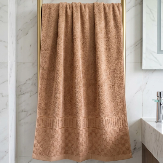 Karmelowo-brzoskwiniowy ręcznik łazienkowy powieszony na złotym grzejniku drabinkowym