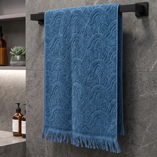 Niebieski, miękki ręcznik frotte Lana o wymiarach 50x100 cm z grubym, tłoczonym wzorem i frędzlami, powieszony w nowoczesnej łazience.