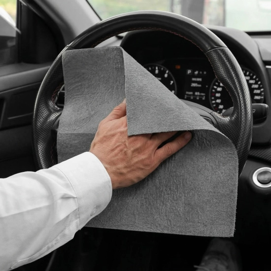 Mężczyzna czyszczący kierownicę i kokpit w samochodzie uniwersalną szarą ściereczką z mikrofibry