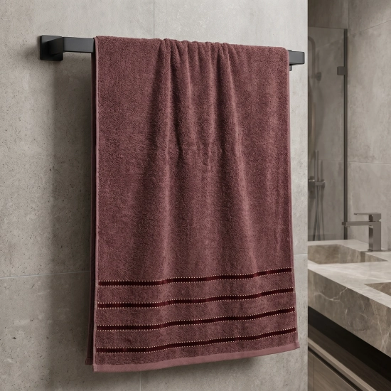 Ręcznik frotte Mondo w odcieniu zgaszonego bordo z elegancką pasiastą bordiurą, wiszący na czarnym, matowym relingu.