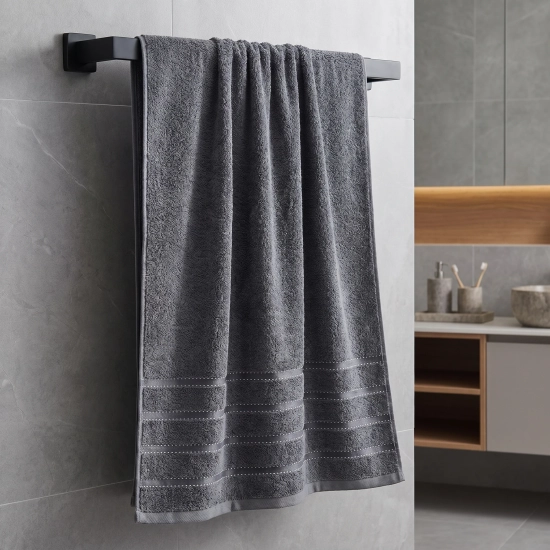 Ciemnoszary ręcznik łazienkowy Mondo 50x100 cm o klasycznym splocie frotte, zawieszony w łazience z ciepłymi, drewnianymi akcentami.