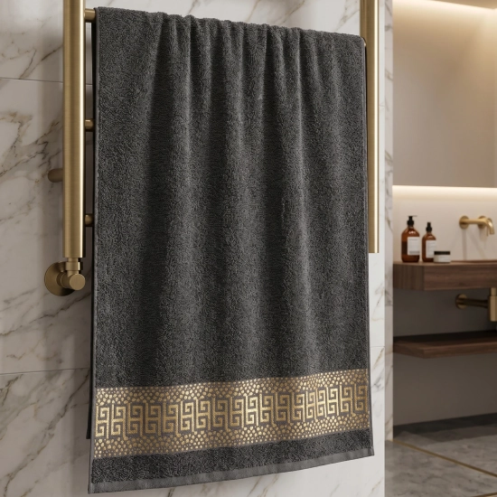 Grafitowy luksusowy ręcznik PERLA ze złotym greckim wzorem wiszący na złotym grzejniku łazienkowym.
