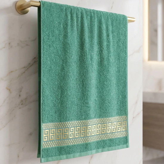 Zielony ręcznik bawełniany PERLA ze złotą ozdobną bordiurą wiszący na uchwycie na tle marmuru.