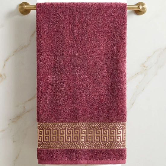 Bordowy ręcznik kąpielowy PERLA w stylu glamour ze złotym greckim wzorem na wieszaku.