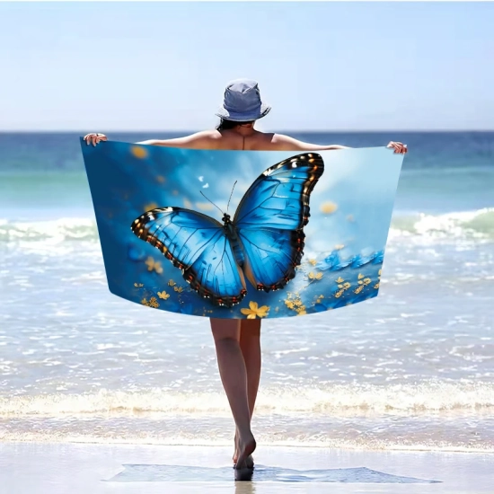 Kobieta w kapeluszu odwrócona tyłem, stojąca w morskiej wodzie i trzymająca rozłożony poziomo szybkoschnący ręcznik plażowy XXL w magiczny wzór motyla