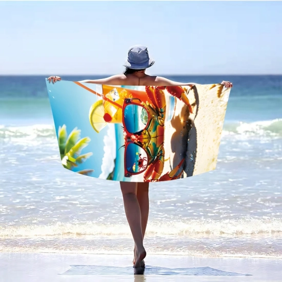 Kobieta w kapeluszu odwrócona tyłem, stojąca w morskiej wodzie i trzymająca rozłożony poziomo szybkoschnący ręcznik plażowy XXL we wzór kraba z koktajlem