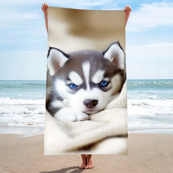 Pionowa prezentacja dużego ręcznika plażowego we wzór słodkiego szczeniaka husky z niebieskimi oczami trzymanego przez osobę stojącą na plaży