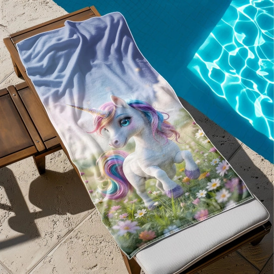 Ręcznik basenowy dla dzieci z mikrofibry z nadrukiem jednorożca rozłożony na drewnianym leżaku tuż obok błękitnej wody basenu. TwójDomNa5.pl