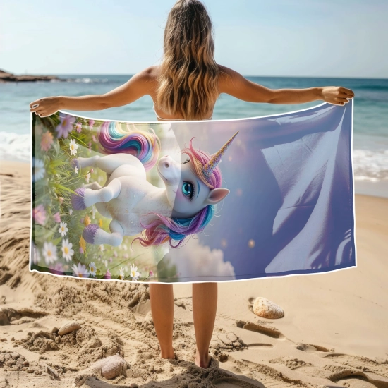 Kobieta na plaży trzymająca rozłożony duży ręcznik plażowy z mikrofibry z nadrukiem magicznego białego jednorożca. Sklep TwójDomNa5.pl