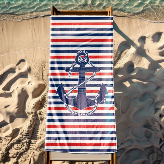 Żeglarski ręcznik plażowy z motywem kotwicy rozłożony na drewnianym leżaku stojącym na piasku nad brzegiem morza.