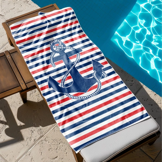 Ręcznik basenowy z mikrofibry z nadrukiem kotwicy na w paski rozłożony na leżaku przy błękitnej wodzie. TwójDomNa5.pl