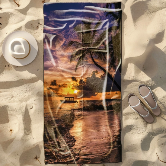 Duży ręcznik plażowy XXL z mikrofibry ze wzorem tropikalnego zachodu słońca, rozłożony na piasku obok białego kapelusza