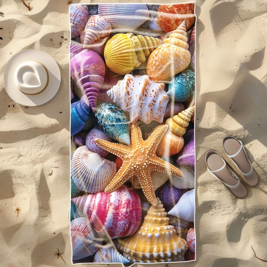Duży ręcznik plażowy XXL z mikrofibry ze wzorem wielokolorowych muszli i rozgwiazdy, rozłożony na piasku obok kapelusza