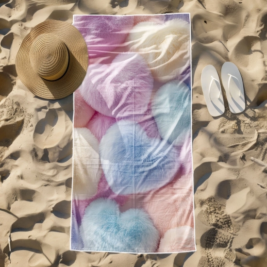 Odporny na piasek ręcznik z mikrofibry o wzorze pastelowych serc leżący obok kapelusza i białych klapek na plaży